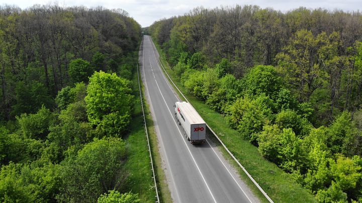 XPO truck driving down a highway with trees on both sides